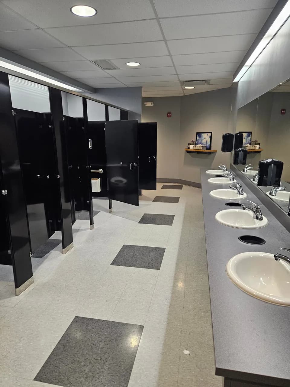 Commercial restroom with a row of sinks, black stall partitions and patterned hard flooring